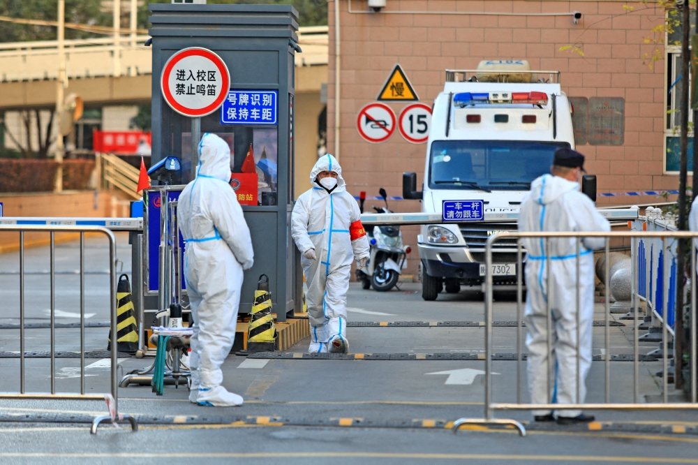 Workers in protective suits stand at an entrance to a university's residential area under lockdown following the coronavirus disease (COVID-19) outbreak in Xian, Shaanxi province, China December 20, 2021. Picture taken December 20, 2021. China Daily via REUTERS/File Photo