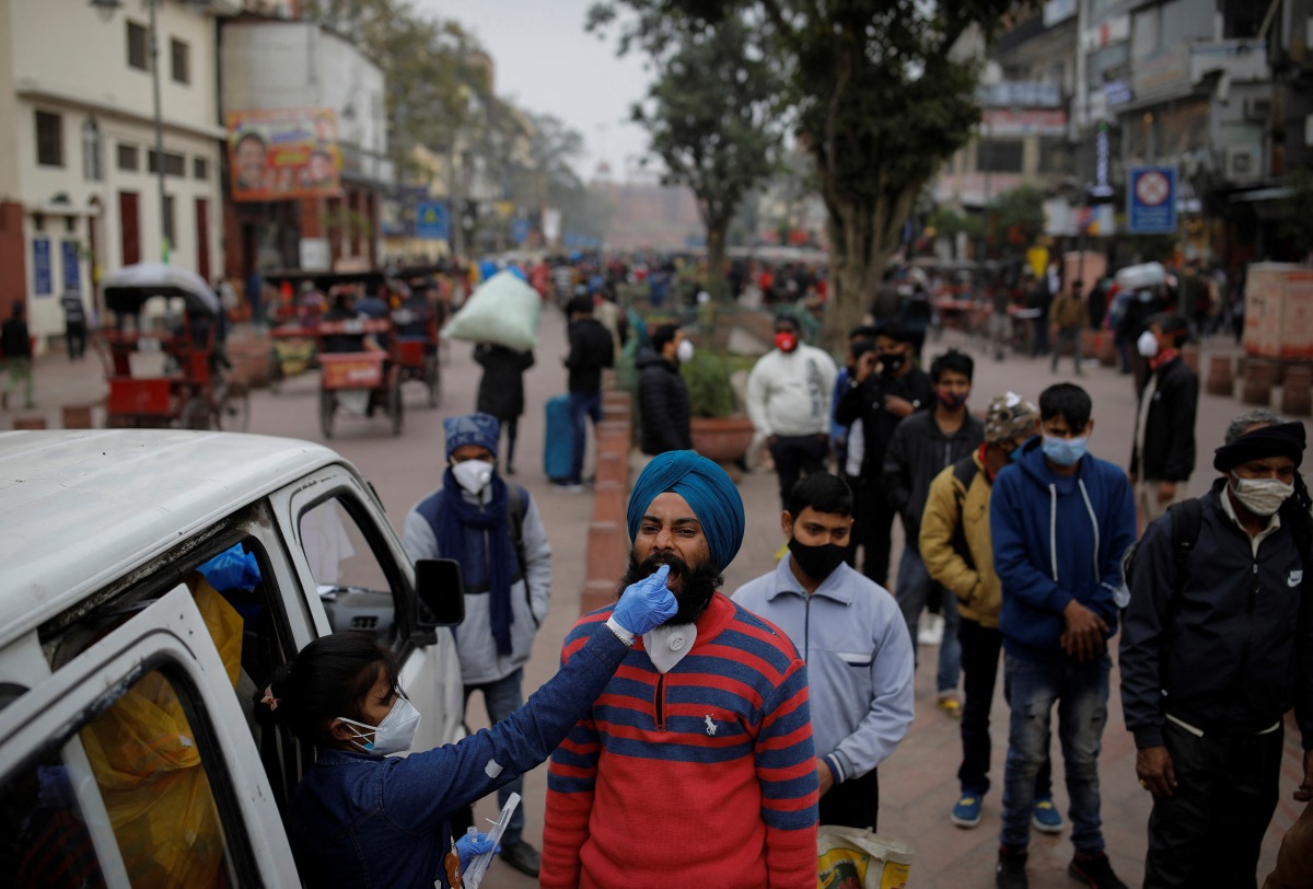 A healthcare worker collects a coronavirus disease (COVID-19) test swab sample from a man as others wait, amidst the spread of the disease, at a market area, in the old quarters of Delhi, India, January 7, 2022. REUTERS/Adnan Abidi
