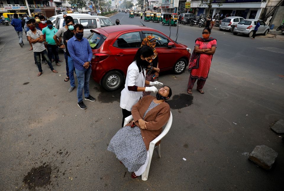 A healthcare worker collects a swab sample from a woman as others wait for their turn during a rapid antigen testing drive for the coronavirus disease (COVID-19) at a roadside in Ahmedabad, India, January 5, 2022. REUTERS/Amit Dave

