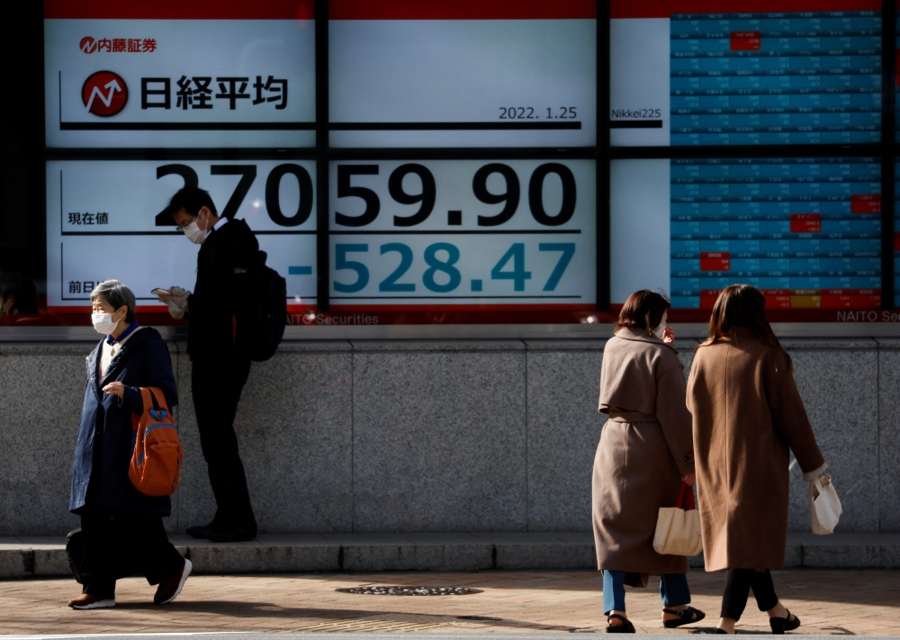 Passersby wearing protective face masks walk past a stock quotation board, amid the coronavirus disease (COVID-19) pandemic, in Tokyo, Japan January 25, 2022. REUTERS/Issei Kato