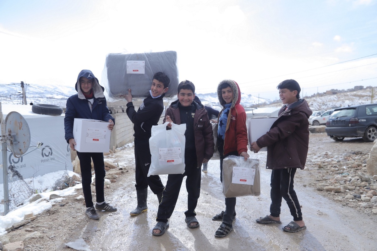 Syrian refugee children in Lebanon carry aid provided by QRCS.