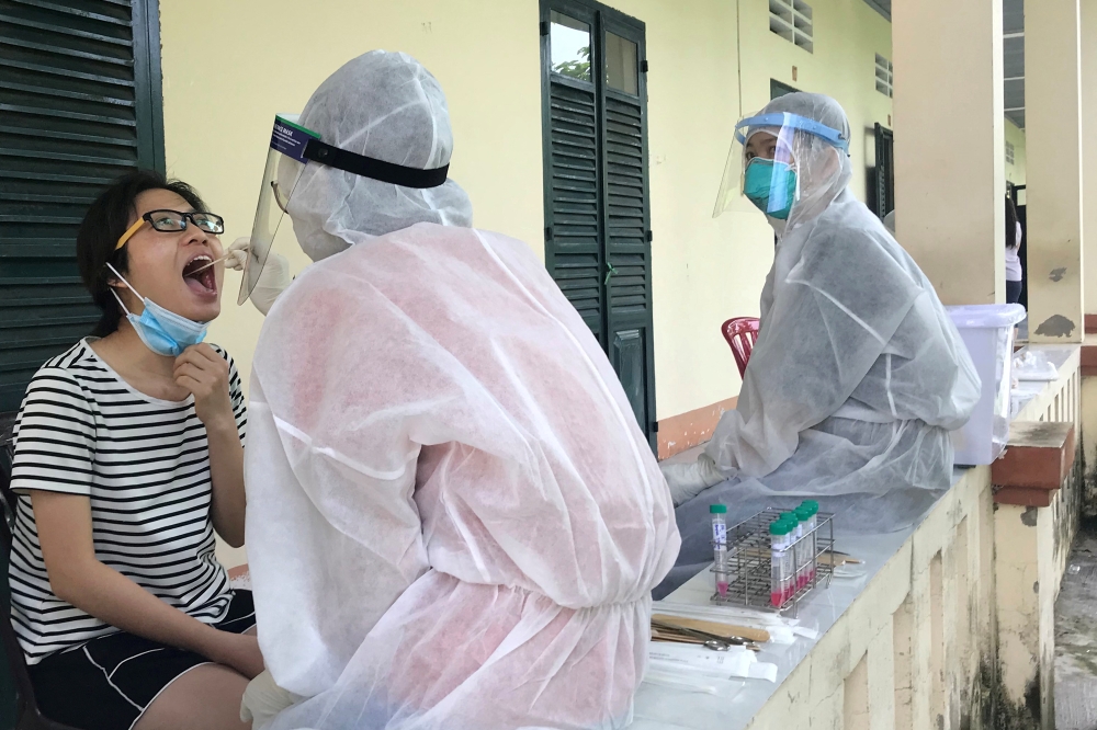 Medical specialists wearing protective hazmat suits take a swab sample to test for the coronavirus disease (COVID-19) from a woman repatriated from Singapore at a military base in southern Mekong delta Dong Thap province, Vietnam August 8, 2020. REUTERS/Mai Nguyen/File Photo
