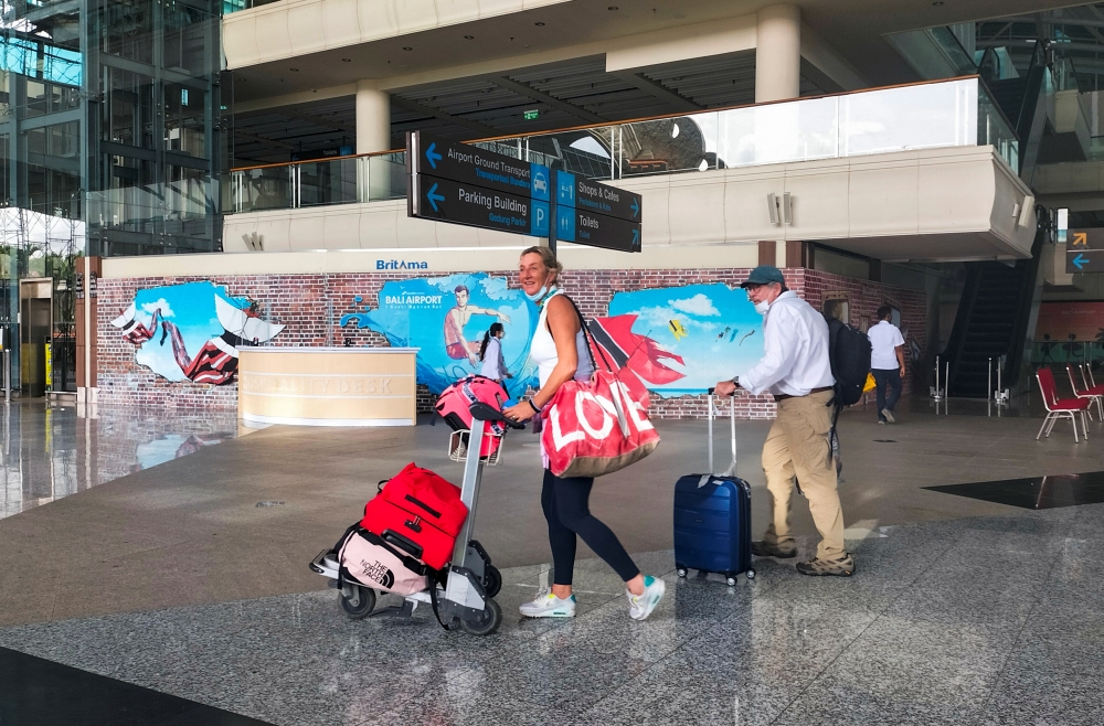 Foreign tourists carrying their luggage walk as they arrive at the I Gusti Ngurah Rai International Airport, as the local government kicks off the first day of the 'quarantine free' trial, amid the coronavirus disease (COVID-19) pandemic, in Bali, Indonesia, March 7, 2022. REUTERS/Sultan Anshori NO RESALES. NO ARCHIVES