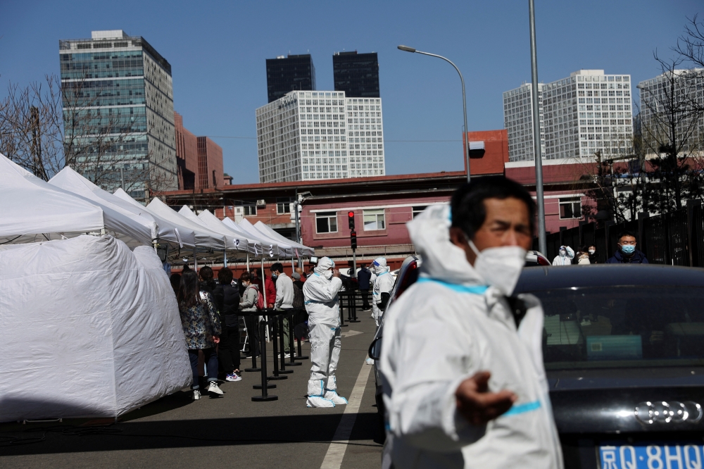 Workers in protective suits stand next to people lining up at a makeshift nucleic acid testing site during a mass testing for the coronavirus disease (COVID-19), in Chaoyang district of Beijing, China March 14, 2022. REUTERS/Tingshu Wang