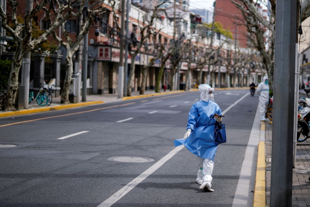 A worker in a protective suit keeps watch on a street, as the second stage of a two-stage lockdown to curb the spread of the coronavirus disease (COVID-19) begins in Shanghai, China April 1, 2022. REUTERS/Aly Song
 