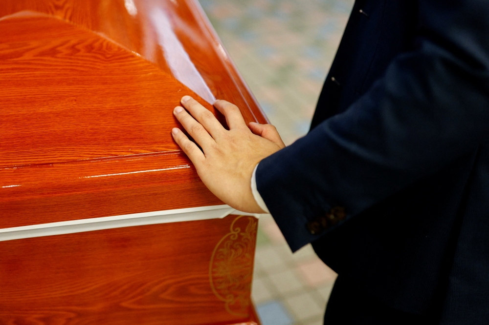 Hades Chan, funeral director of YuXiang Funeral Company, places his hand over a coffin of coronavirus disease (COVID-19) victim before cremation, in Hong Kong, China, April 1, 2022. Reuters/Tyrone Siu
