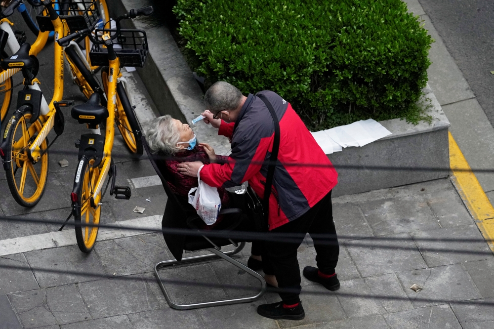 A man helps a woman to consume a packet of traditional Chinese medicine (TCM) Lianhua Qingwen, as she sits by the side of a road outside a residential compound, during a lockdown to curb the spread of the coronavirus disease (COVID-19) in Shanghai, China April 5, 2022. REUTERS/Aly Song