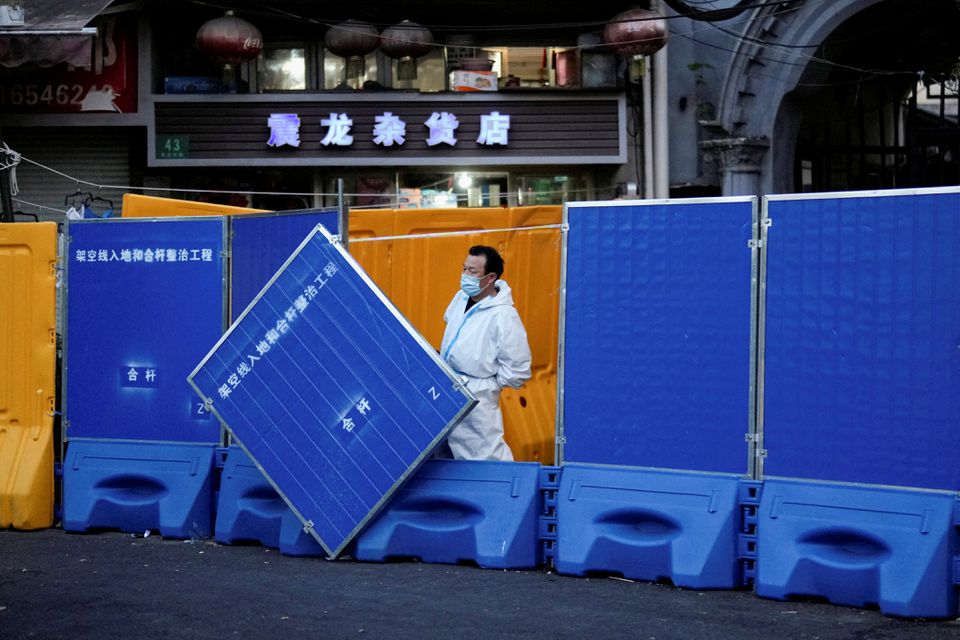 A worker in a protective suit keeps watch next to barricades set around a sealed-off area, during a lockdown to curb the spread of the coronavirus disease (COVID-19) in Shanghai, China April 11, 2022. REUTERS/Aly Song

