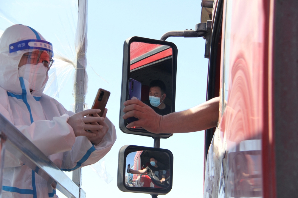 A police officer in a protective suit checks the information of a truck driver at a toll gate of a highway following the coronavirus disease (COVID-19) outbreak, in Fuxin, Liaoning province, China April 15, 2022. cnsphoto via REUTERS
