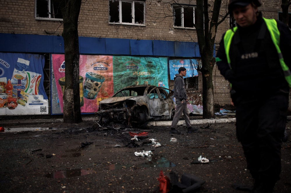 People walk past a destroyed car, following Russian shelling, as Russia's attack on Ukraine continues, in Kharkiv, Ukraine, April 18, 2022. REUTERS/Alkis Konstantinidis
