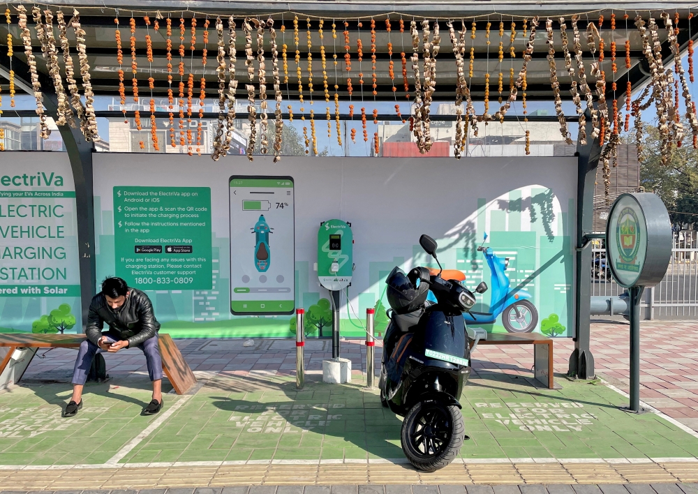 A man checks his mobile phone as he waits while recharging his Ola electric scooter at an electric vehicle charging station in New Delhi, India, February 12, 2022. REUTERS/Aditi Shah//File Photo