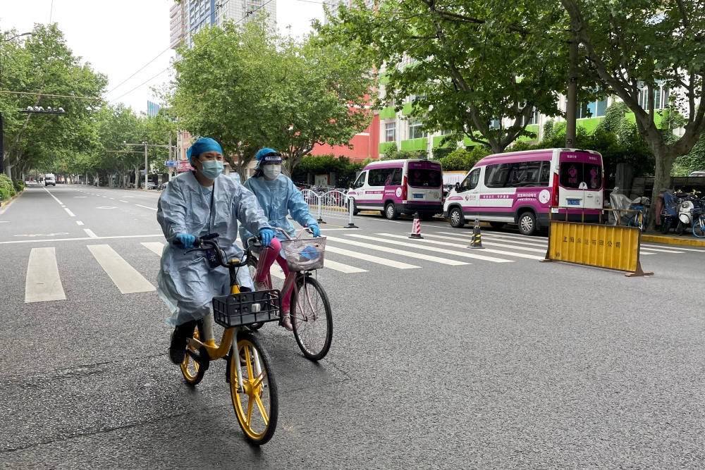 Workers in protective suits ride bicycles on a street amid a coronavirus disease (COVID-19) outbreak, during the Labour Day holiday in Shanghai, China April 30, 2022. REUTERS/Brenda Goh