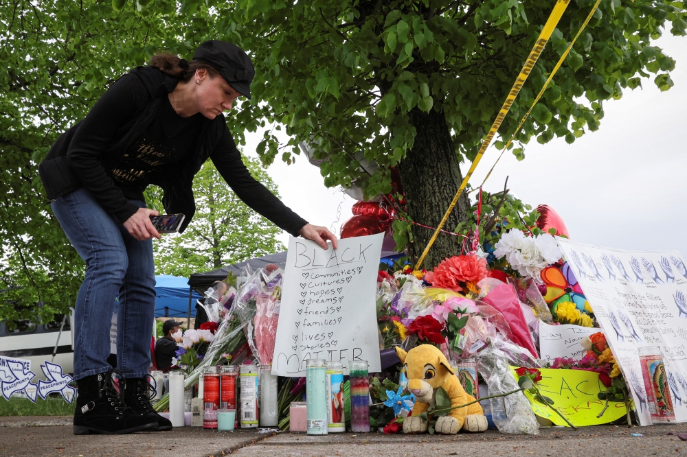 A woman places a sign at a memorial for victims near the scene of a shooting at a Tops supermarket in Buffalo, New York, U.S. May 16, 2022. REUTERS/Brendan McDermid