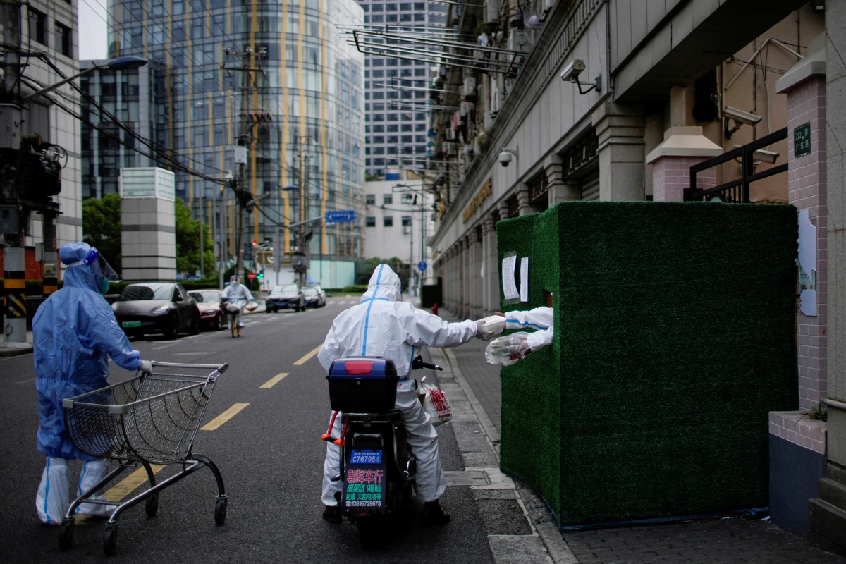 A worker in a protective suit passes food through a gap in the barrier at a residential area during lockdown, amid the coronavirus disease (COVID-19) pandemic, in Shanghai, China, May 26, 2022. REUTERS/Aly Song
