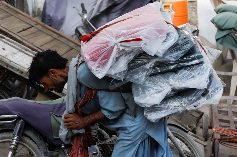 A labourer carries packs of textile fabric to deliver to a nearby shop in a market in Karachi, Pakistan, on June 24, 2022. (Reuters/Akhtar Soomro)