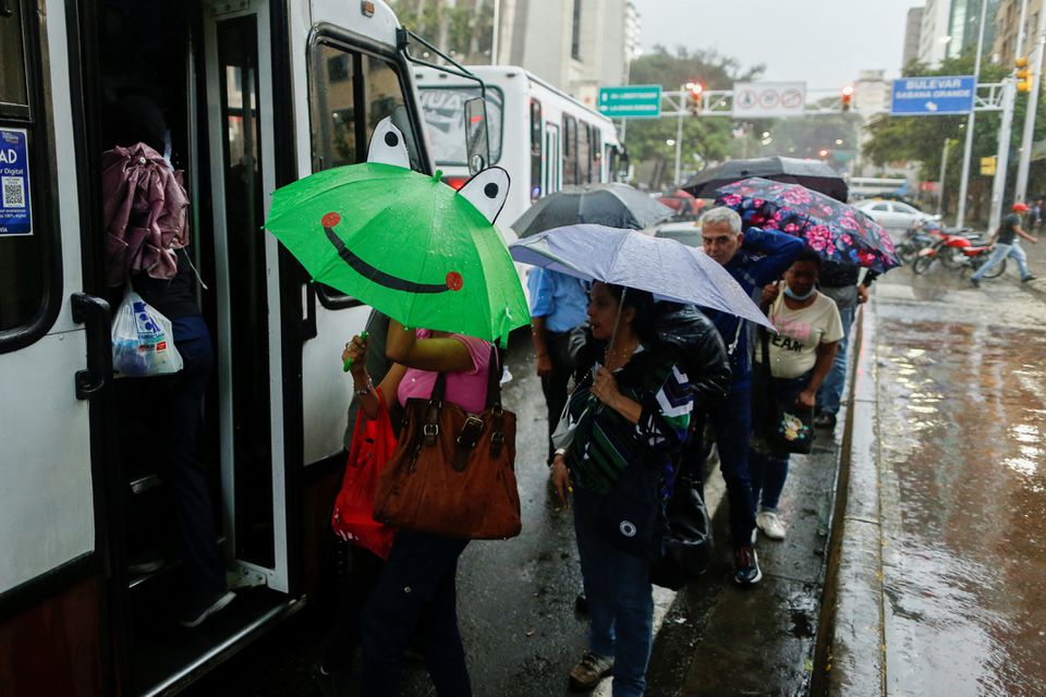 People in a line to board a bus use umbrellas to cover from the rain caused by Potential Tropical Cyclone Two, which the U.S. National Hurricane Center says will likely develop into tropical storm Bonnie, as it passes through the Caribbean, in Caracas, Venezuela June 29, 2022. REUTERS/Leonardo Fernandez Viloria