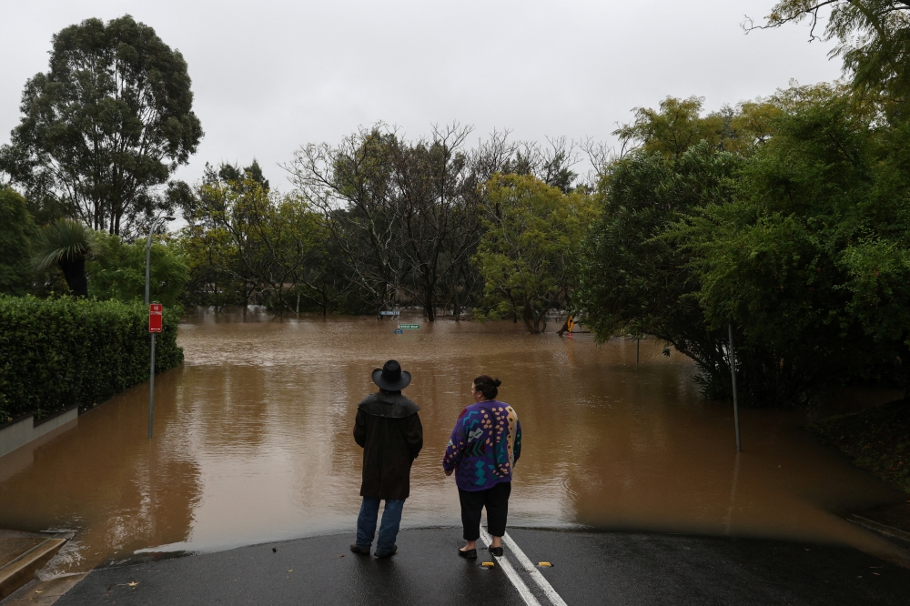 Onlookers stand at the edge of floodwaters on a residential street following heavy rains in the Windsor suburb of Sydney, Australia, July 5, 2022. REUTERS/Loren Elliott