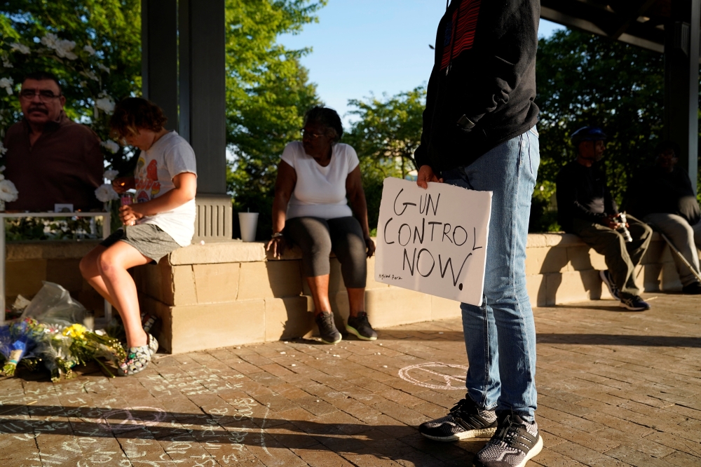 A mourner holds a sign advocating for gun control while visiting a memorial for victims of a mass shooting at a Fourth of July parade in the Chicago suburb of Highland Park, Illinois, US, on July 7, 2022. (Reuters/Cheney Orr)