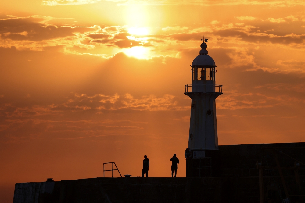 People stand on Mevagissey Harbour wall as the sun rises in Mevagissey Harbour in Cornwall, Britain, July 18, 2022. REUTERS/Tom Nicholson