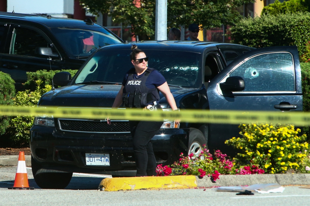 A police officer walks next to a car with bullet holes on the windows at a crime scene after authorities alerted residents of multiple shootings targeting transient victims in the Vancouver suburb of Langley, British Columbia, Canad, July 25, 2022. (REUTERS/Jesse Winter)