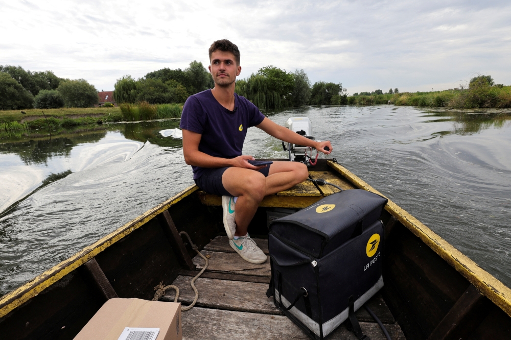 A postman of French postal service company La Poste distributes letters and parcels from a boat to residents who live in Salpwerick around the Marais Audomarois, France, July 28, 2022.  REUTERS/Pascal Rossignol