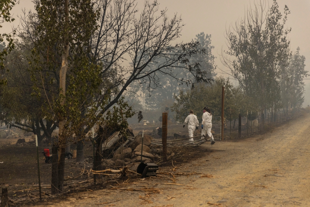 Forensic anthropologists walk into a property to look for human remains in a damaged vehicle as the McKinney Fire burns near Yreka, California, U.S., August 1, 2022. REUTERS/Carlos Barria