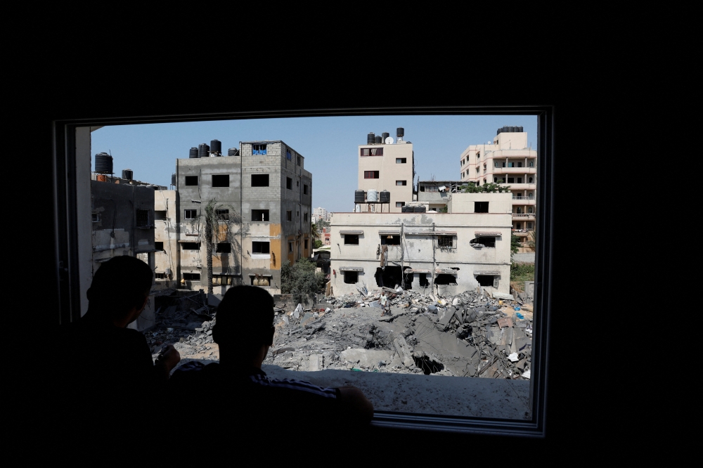 Palestinians look through a damaged window at the rubble of a house destroyed in an Israeli air strike in Gaza City on August 6, 2022. (Reuters/Ibraheem Abu Mustafa)