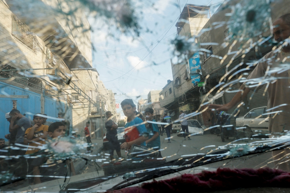 Palestinians, seen through a damaged car window, gather on a street amid Israel-Gaza fighting, in the northern Gaza Strip August 7, 2022. REUTERS/Mohammed Salem