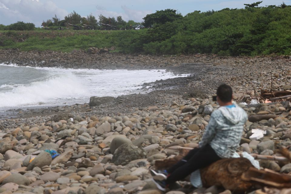 An onlooker takes images as soldiers take part in an annual live fire military exercise with 155mm howitzers while a man uses his cellphone to take images by the shore in Pingtung county, southern Taiwan August 9, 2022. REUTERS/Ann Wang


