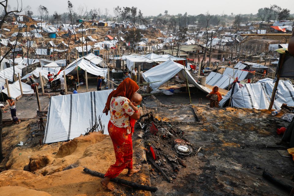 A Rohingya refugee woman carries her child after a massive fire broke out two days ago in Cox's Bazar, Bangladesh, March 24, 2021. REUTERS/Mohammad Ponir Hossain

