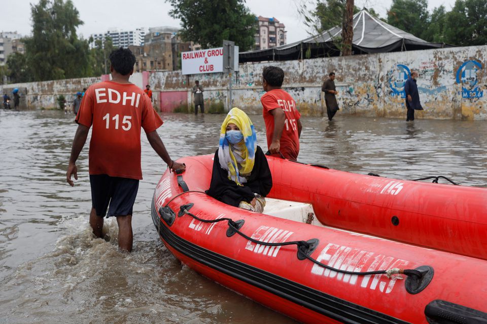 A woman sits in a rubber boat as volunteers pull through a flooded road during the monsoon season in Karachi, Pakistan July 9, 2022. REUTERS/Akhtar Soomro


