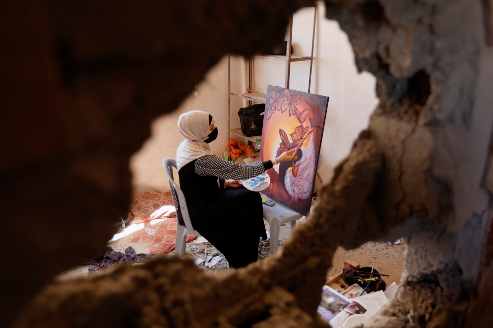 A Palestinian artist draws a painting inside the damaged house of Gaza artist, Duniana Al-Amour, who had been killed during Israel-Gaza fighting, in Khan Younis in the southern Gaza Strip, August 23, 2022. (REUTERS/Ibraheem Abu Mustafa)