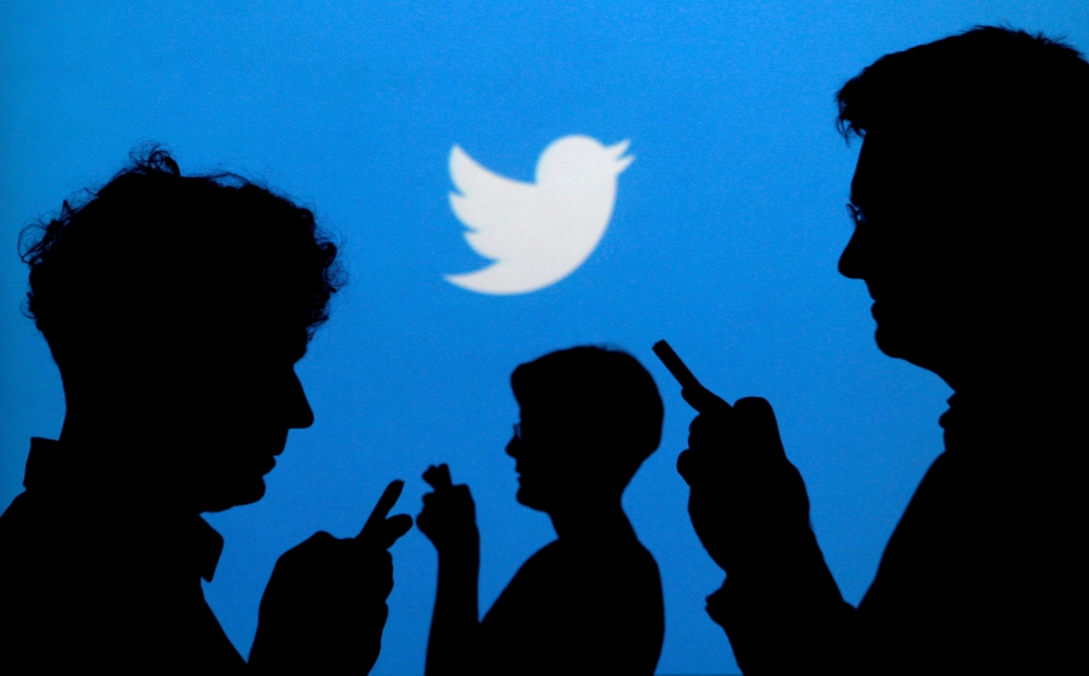 People holding mobile phones are silhouetted against a backdrop projected with the Twitter logo in this illustration picture taken on September 27, 2013. File Photo / Reuters