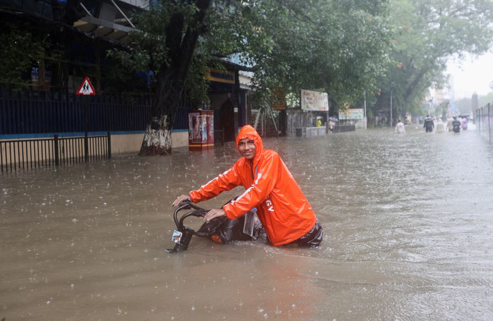 A man wades through a flooded street with his bike amidst heavy rainfall in Mumbai, India, July 5, 2022. (REUTERS/Francis Mascarenhas)