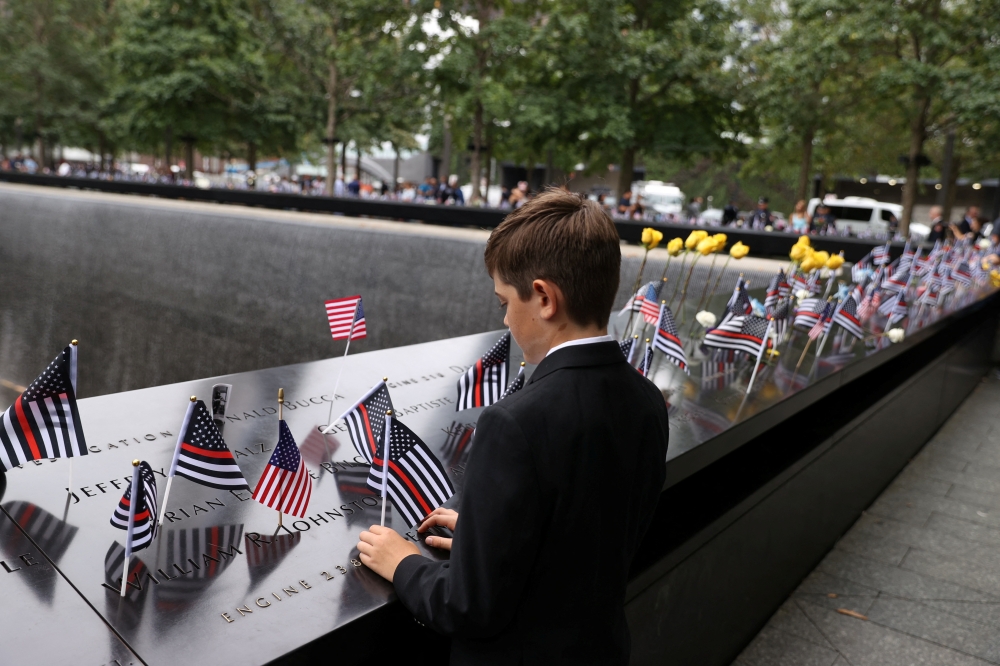 A boy places a flag during a ceremony marking the 21st anniversary of the September 11, 2001 attacks on the World Trade Center at the 9/11 Memorial and Museum in the Manhattan borough of New York City, on September 11, 2022. REUTERS/Amr Alfiky