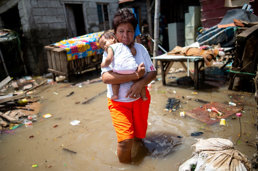 A woman carries a child as she wades through the flood caused by Super Typhoon Noru, in San Ildefonso, Bulacan province, Philippines, September 27, 2022. REUTERS/Lisa Marie David