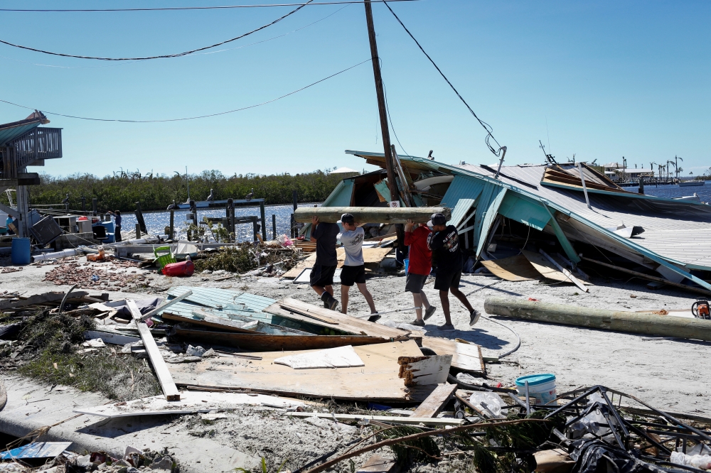 Men carry a wood log in a destroyed marina after Hurricane Ian caused widespread destruction in Fort Myers Beach, Florida, U.S., September 30, 2022. Reuters/Marco Bello