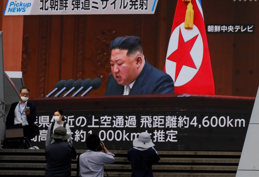 People walk in front of a screen showing North Korea's leader Kim Jong Un in a news report about North Korea firing a ballistic missile over Japan, in Tokyo on October 4, 2022. REUTERS/Issei Kato