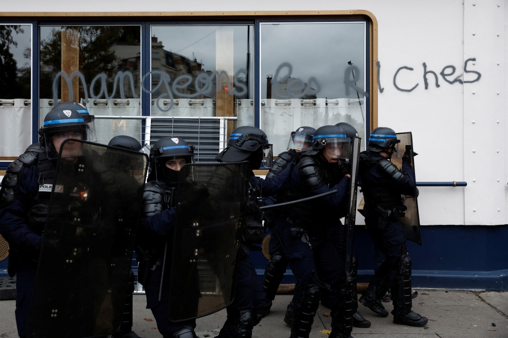 French CRS riot police secure a position during a demonstration in Paris as part of a nationwide day of strike and protests for higher wages and against requisitions at refineries in France, on October 18, 2022. The slogan reads 
