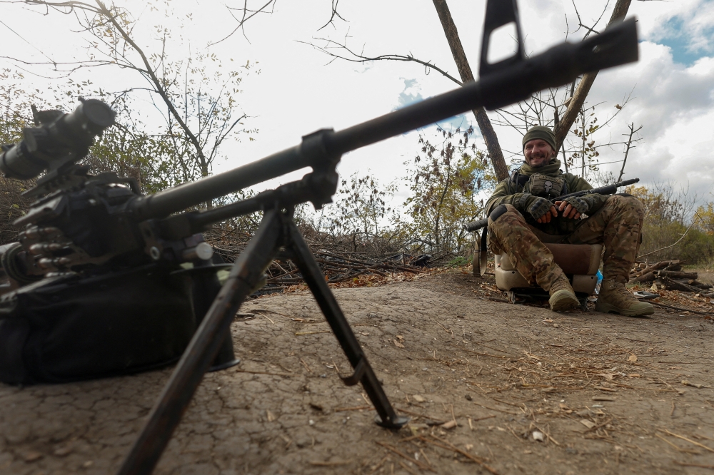 Ukrainian serviceman Yuriy smiles next to a machine gun captured from Russian troops at a position on a frontline in Mykolaiv region, Ukraine October 21, 2022. Reuters/Valentyn Ogirenko 