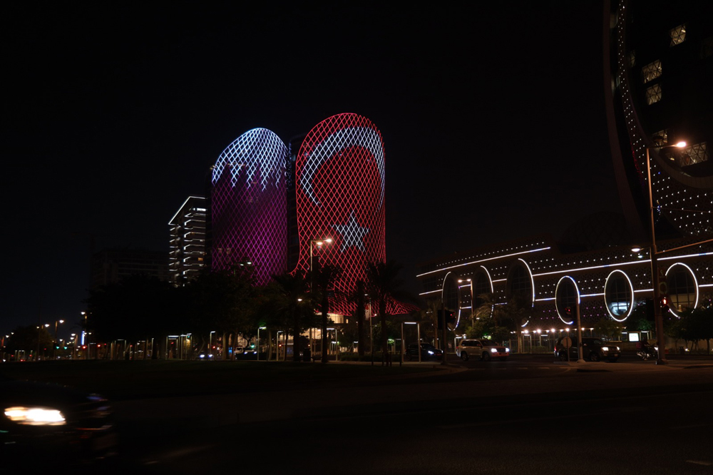 A building in Doha lit up with Qatar and Turkiye flags. 
