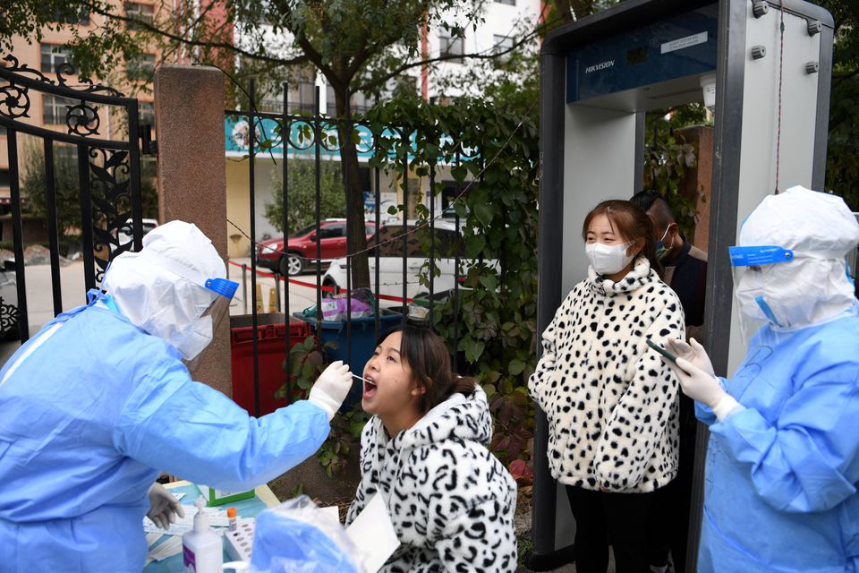 A medical worker in protective suit collects a swab from a resident at a free nucleic acid testing site following new cases of the coronavirus disease (COVID-19), in Lanzhou's Chengguan district, Gansu province, China October 20, 2021. cnsphoto via REUTERS

