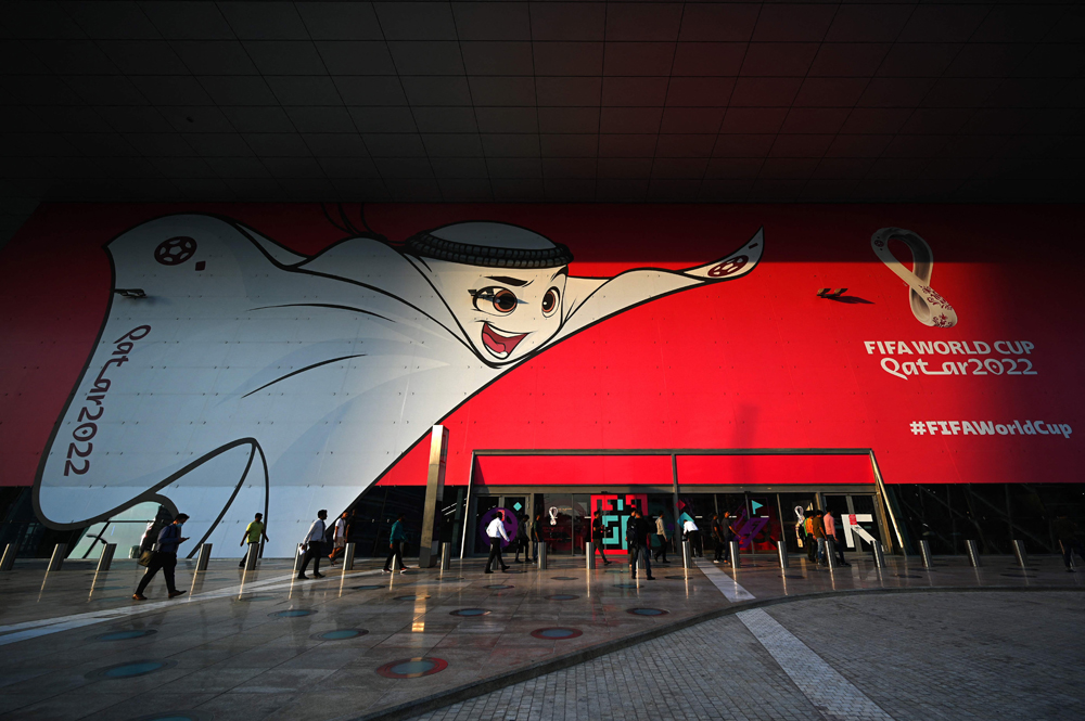 People walk past a poster of Qatar 2022 mascot La’eeb in Doha, yesterday. (AFP)