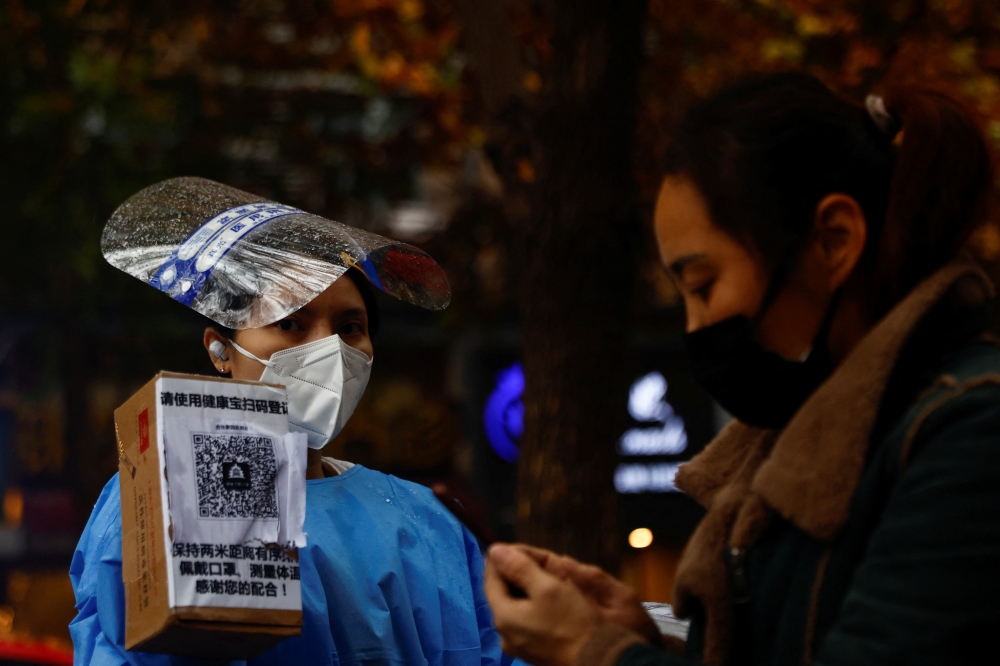 A worker in a protective suit guides people to scan health QR code at a nucleic acid test booth for the coronavirus disease (COVID-19), in Beijing, China November 11, 2022. Reuters/Tingshu Wang