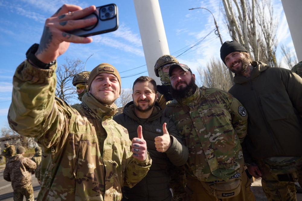 This handout photograph taken and released by Ukrainian Presidential press service on November 14, 2022, shows Ukrainian President Volodymyr Zelensky (2nd left) posing for a selfie with Ukrainian servicemen during his visit to the newly liberated city of Kherson, following the retreat of Russian forces from the strategic hub. (Ukrainian Presidential Press Service / AFP) 