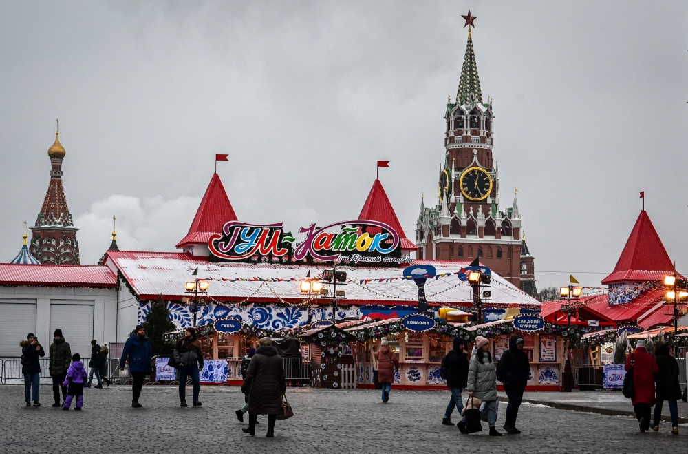 People walk past the Christmas fair on Red square near the Spasskaya tower of the Kremlin and the Saint Basil Cathedral in Moscow on November 28, 2022. (Photo by Yuri KADOBNOV / AFP)