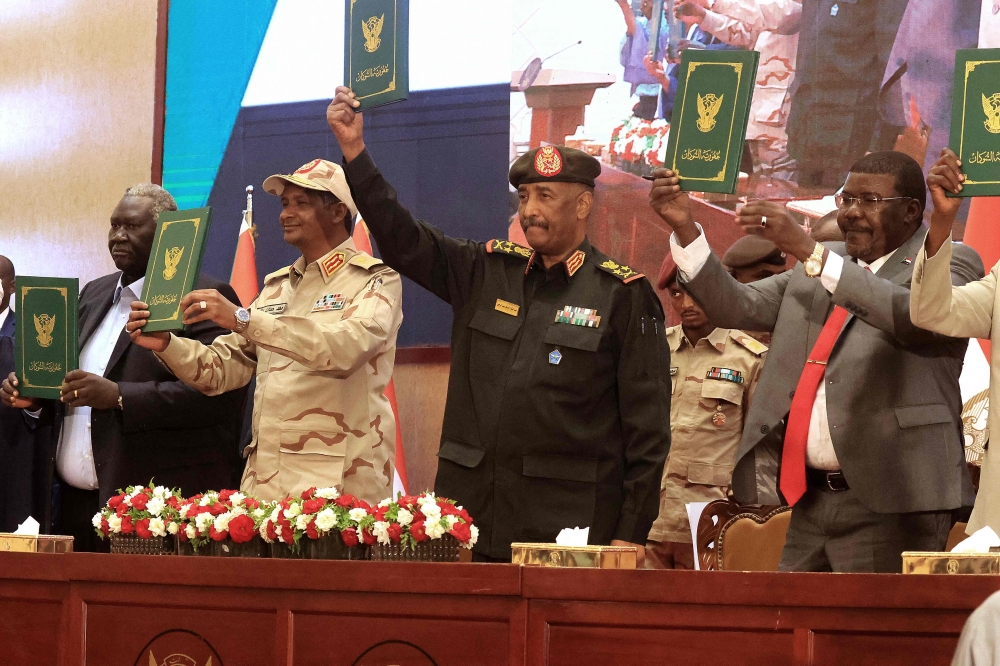 Sudan's Army chief Abdel Fattah al-Burhan (center right) and paramilitary commander Mohamed Hamdan Dagalo (center left) lift documents alongside civilian leaders following the signing of an initial deal aimed at ending a deep crisis caused by last year's military coup, in the capital Khartoum on December 5, 2022. (Photo by ASHRAF SHAZLY / AFP)
 