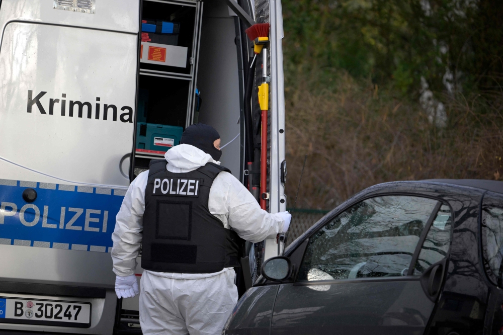 A policeman stands behind a car of the forensic experts during a raid on December 7, 2022 in Berlin. Photo by Tobias Schwarz / AFP