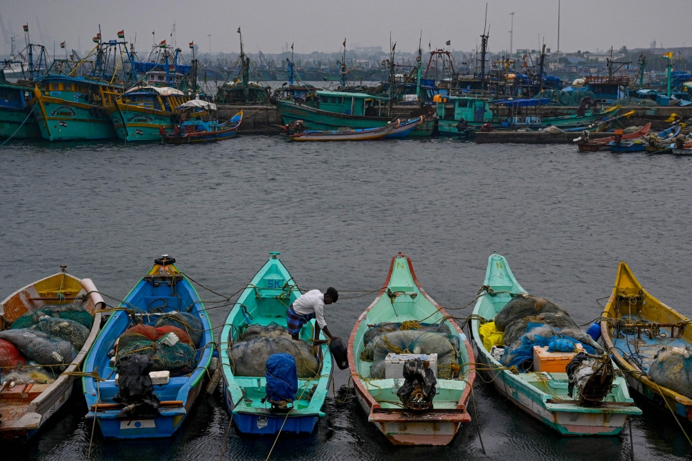 A fisherman moors his boat amid high tide as dark clouds loom over the Kasimedu fishing harbor in Chennai on December 8, 2022, ahead of Cyclone Mandous forecasted landfall in north Tamil Nadu-south Andhra Pradesh coasts. (Photo by Arun SANKAR / AFP)