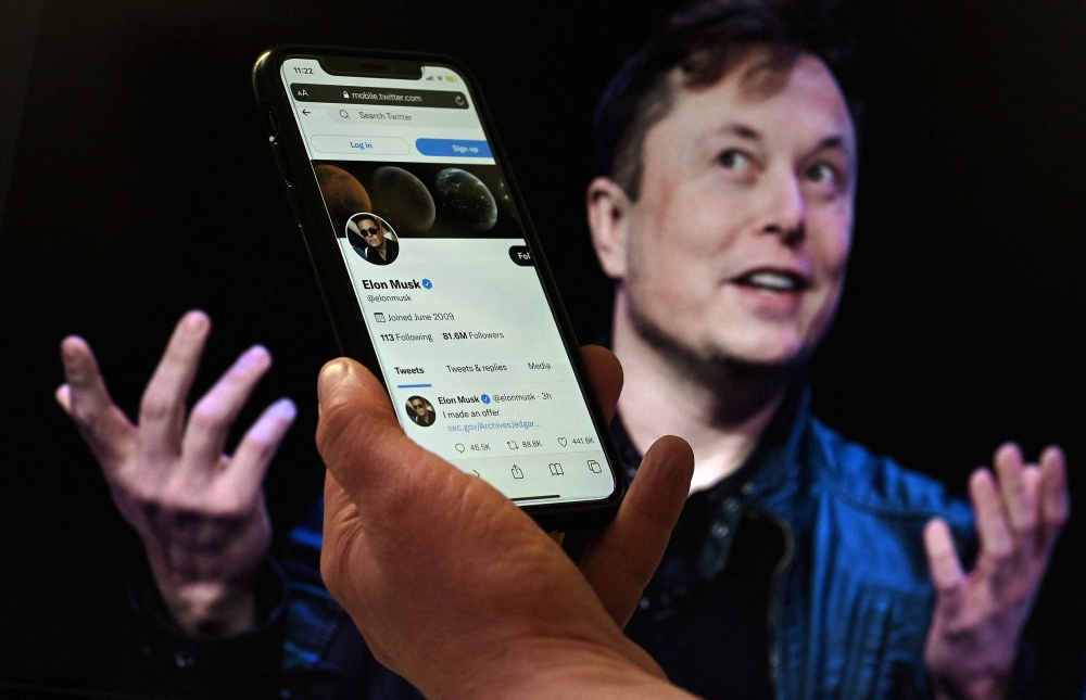In this file photo taken on April 14, 2022 a phone screen displays the Twitter account of Elon Musk with a photo of him shown in the background, in Washington, DC. (Photo by Olivier Douliery / AFP)
